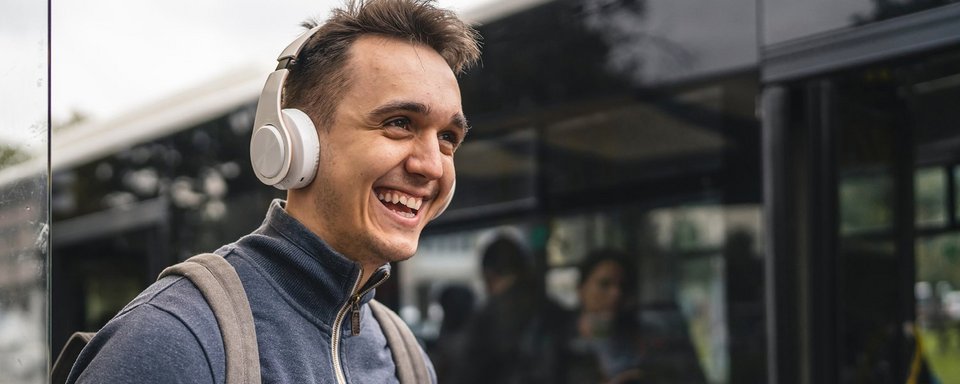 Junger Mann mit Kopfhörer und Handy beim Einsteigen in den Bus