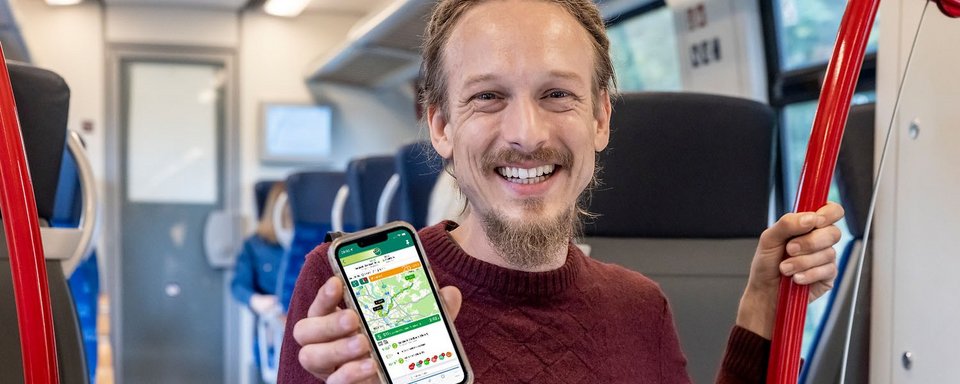 Fahrgast im Zug zeigt VRS-App im Handy-Display 